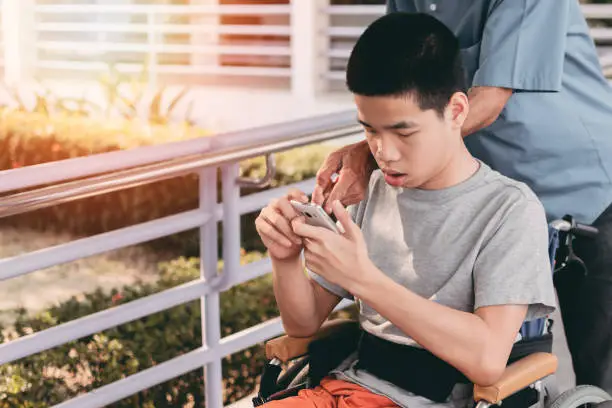 Photo of Young man with disabilities on wheelchair using mobile phone, Technology for life concept.