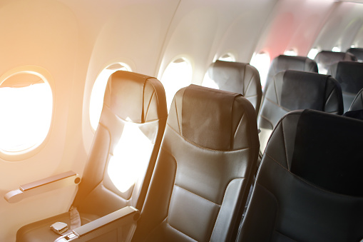 Empty dark seats in the back inside airplane with sunset light in windows . Peaceful and tranquil row of seats in commercial plane cabin. Airplane interiors. High quality photo.