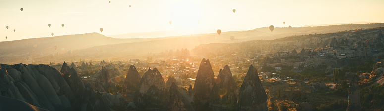 Golden sunrise over Goreme town in Cappaocia front side sunlight directional with balloons on air in sunny hazy autumn calm morning