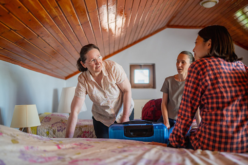 A host-mother is welcoming and showing bed room to two multi-ethnic female tourist guests for home-staying.