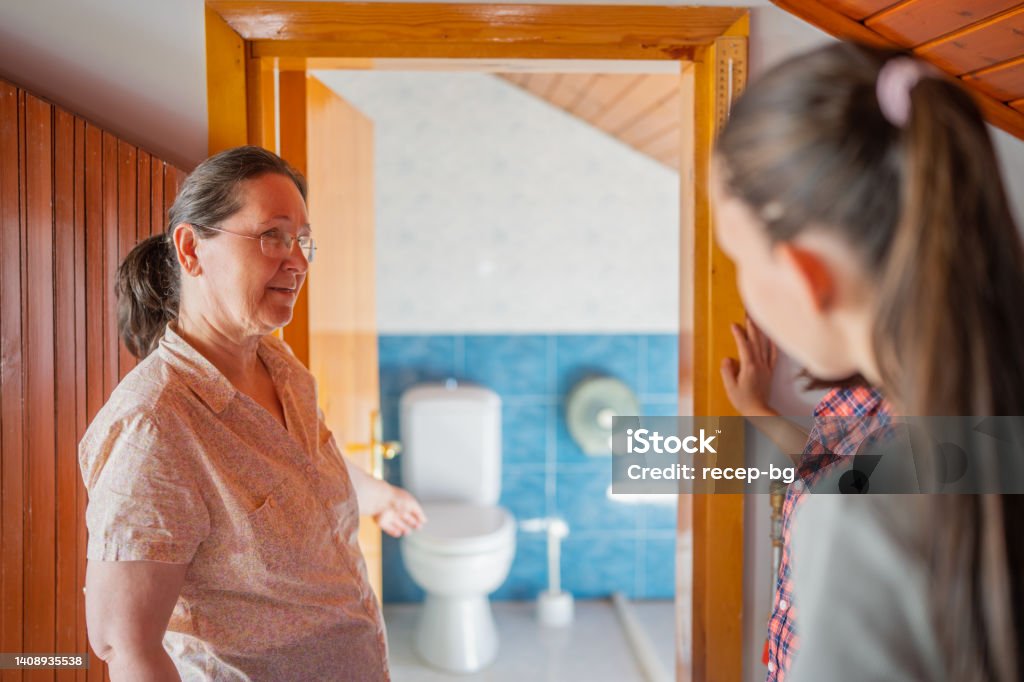 Host-mother welcoming and showing bed room and toilet and bathroom to two multi-ethnic female tourist guests for home-staying A host-mother is welcoming and showing bed room and toilet and bathroom to two multi-ethnic female tourist guests for home-staying. Greeting Stock Photo