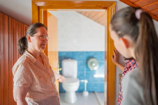 Photo of Host-mother welcoming and showing bed room and toilet and bathroom to two multi-ethnic female tourist guests for home-staying