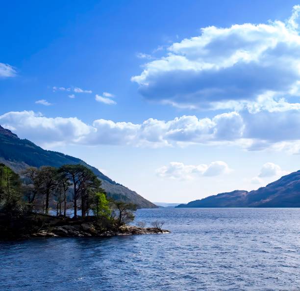 Beautiful Loch Lomond, Scottish Highlands. Calm water and blue sky with clouds. Bit of land with trees jutting out into the lake. Peaceful, serene scenic view. Scotland, UK.
