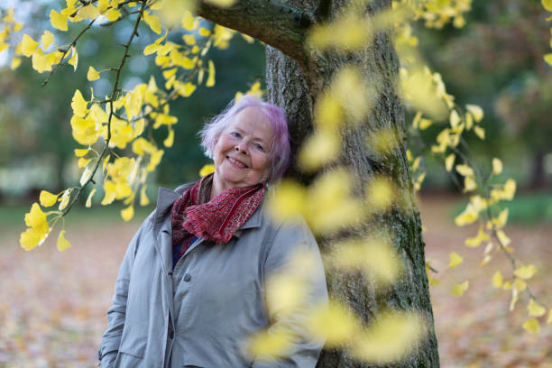 istock Senior woman outdoors in atumn leaning at Ginkgo Tree 1408941982