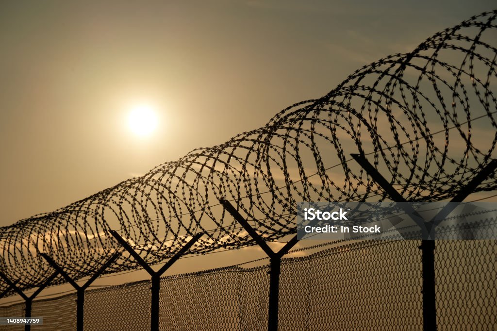 Border fence from an airport. Security device made of round steel wire protects. Backlight in the evening. Prison Stock Photo