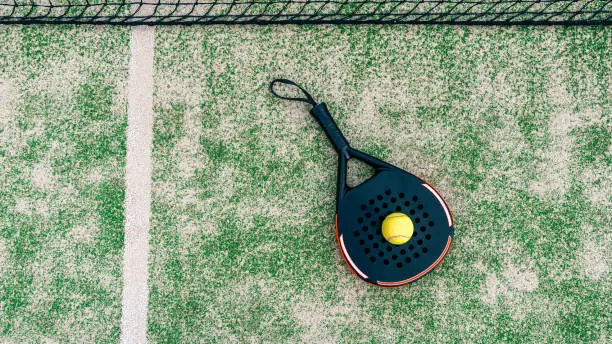 Yellow ball on top of the padel racket and behind net on a green court grass turf outdoors. Paddle is a racquet game. Professional sport concept with space for text