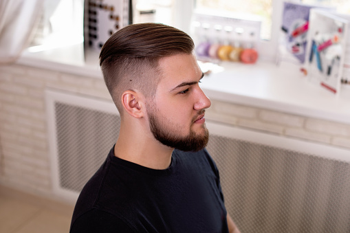 Young stylish man with fashion haircut on barbershop background
