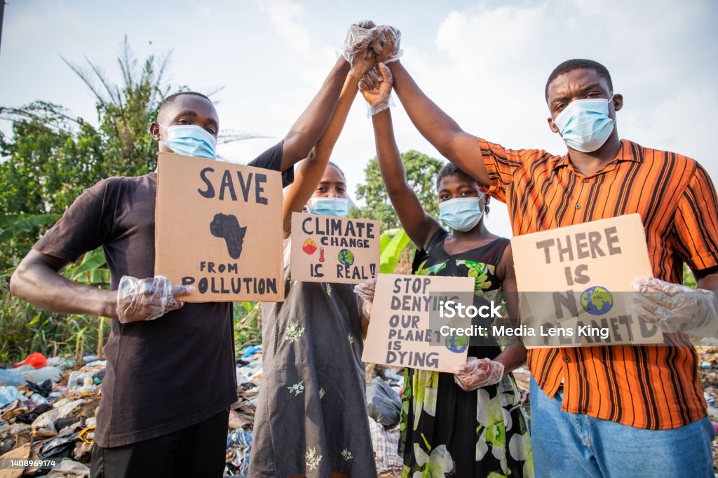 Four young adults protest with signs against pollution outside an illegal open landfill in Africa. Four young adults protest with signs against pollution outside an illegal open landfill in Africa Climate Change Stock Photo