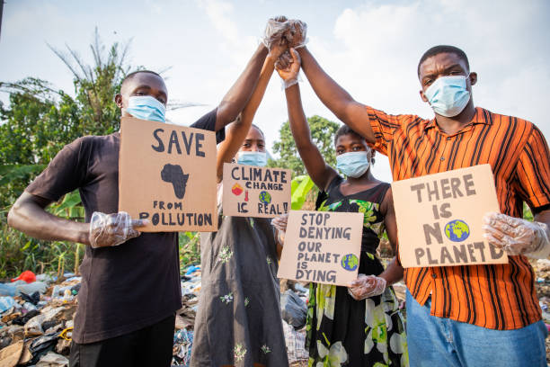 Four young adults protest with signs against pollution outside an illegal open landfill in Africa. Four young adults protest with signs against pollution outside an illegal open landfill in Africa cameroon photos stock pictures, royalty-free photos & images