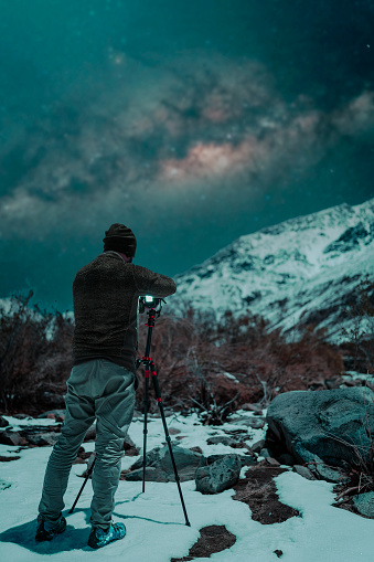 photographer in the snow at night taking pictures of the stars and milky way on the snowy mountain