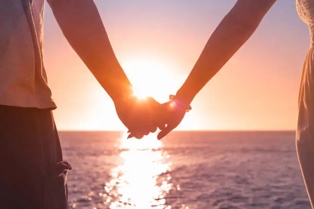 Couple holding hands on beach at sunset.