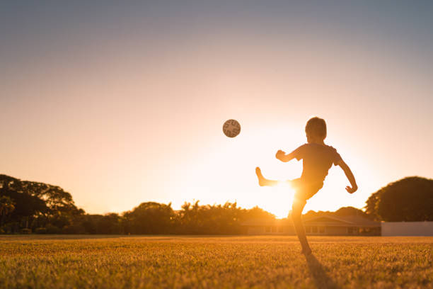 garçon jouant au football au coucher du soleil. - nature summer child one little boy photos et images de collection