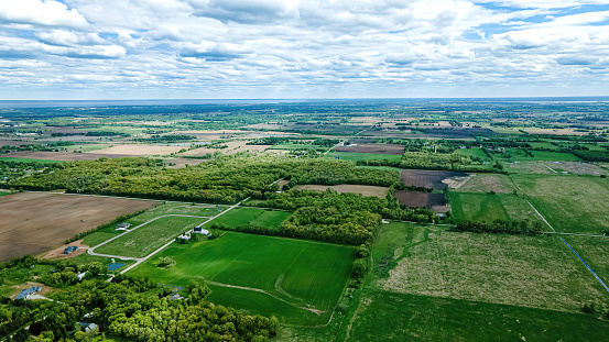 Rural farmlands, fields, and meadows as far as the horizon under a cloudy blue sky