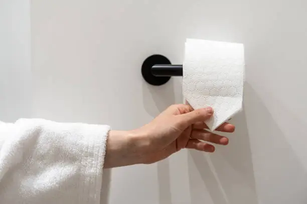Cropped view of woman hand take piece of toilet paper with folded corner. Woman hold roll of soft hygienic tissue. Hygienic concepts in hotel, home and public restrooms