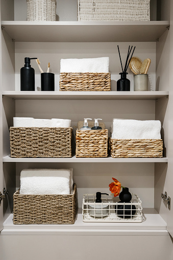 Household items, toilet paper rolls, white bath towels and cosmetics bottles on shelves in the bathroom cabinet Organization of space in wardrobe. Bedding, linen, home perfumes and folded bathrobes
