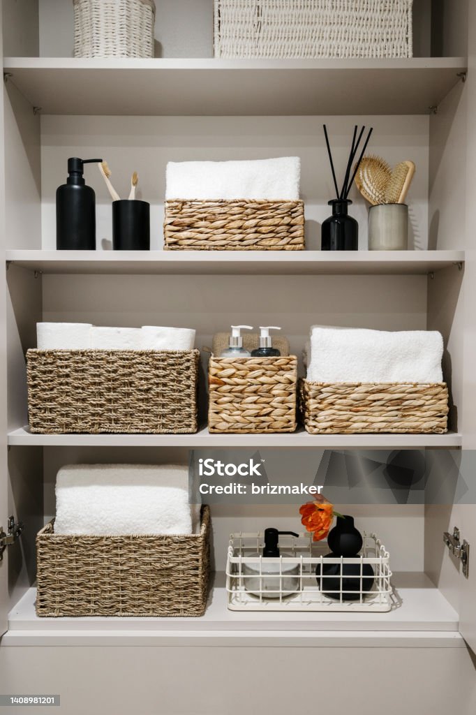 Bathroom cabinet with toilet paper rolls, white bath towels and cosmetics bottles Household items, toilet paper rolls, white bath towels and cosmetics bottles on shelves in the bathroom cabinet Organization of space in wardrobe. Bedding, linen, home perfumes and folded bathrobes Bathroom Stock Photo