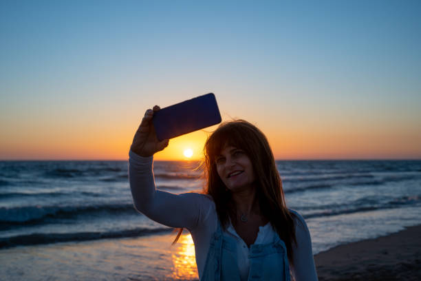 istock smiling woman taking a selfie with a sunset on the beach 1408982245