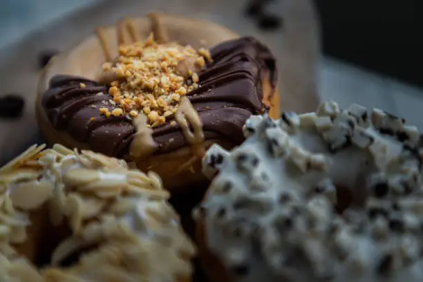 Close-up of Three doughnuts covered with Choco peanut butter, Cookies and creme and Almendras and on wooden cutting board. The concept of delicious glazed donuts, Space for text, Selective Focus.
