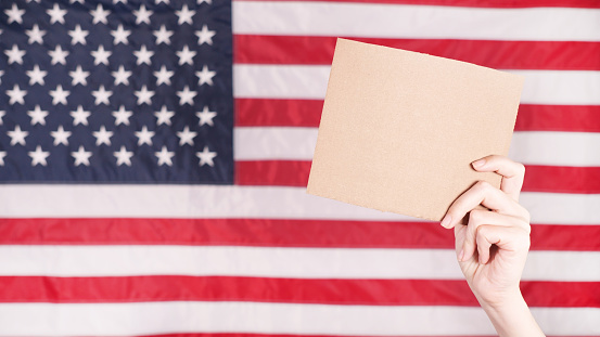 Young woman holding blank sign in her hands close up. American flag on background