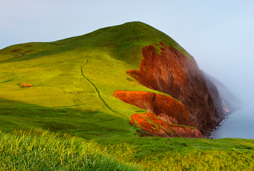 Eroded red cliff with hiking trail at sunrise on a foggy morning