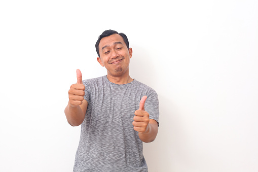 Portrait of Asian man stand happy and positive with thumbs up approving with a big smile and funny face expressing okay gesture isolated over white background