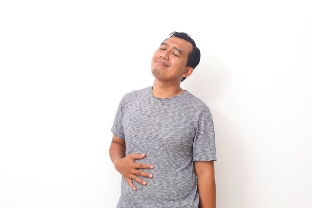 asian man feel very full after eating too much food. the man holds his stomach full of food. isolated on white background - full contact imagens e fotografias de stock