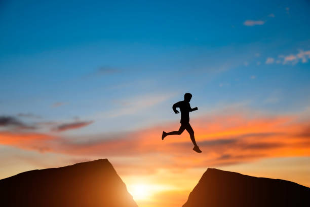 istock Young man jumping over precipice between two mountains at sunrise. Freedom, risk, challenge, success. 1409003926
