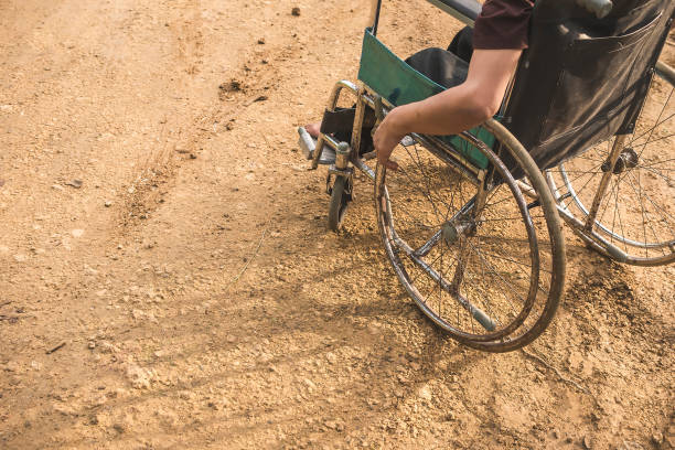 An anonymous paraplegic man on his old wheelchair with his hands resting on the handrims. Traveling on a dirt road. An anonymous man with a disability caused by childhood polio. A wheelchair user with his hands resting on the handrims. Traveling on a dirt road. polio virus photos stock pictures, royalty-free photos & images