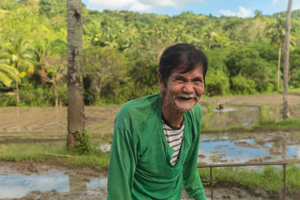 istock An old and friendly asian farmer laughs while at a rice paddy. Rural countryside scene. 1409007795