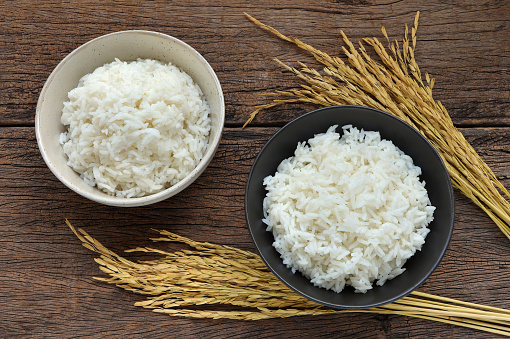 White rice in bowl and ear of rice on a wooden background. Steam rice in white and black bowl. Top view