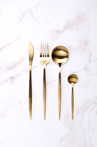 Clean golden metal cutlery on light marble background. Design concept. Top view.