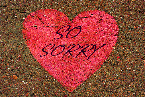 So Sorry text on heart shape painted on textured asphalt surface