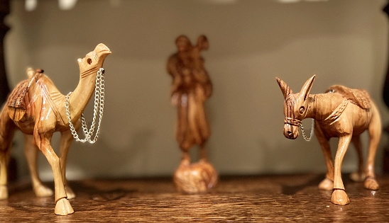 Wooden figurines of a donkey and a camel stand on both sides of the photo. In the center, in full blur, is the figure of a man on his back with a lamb
