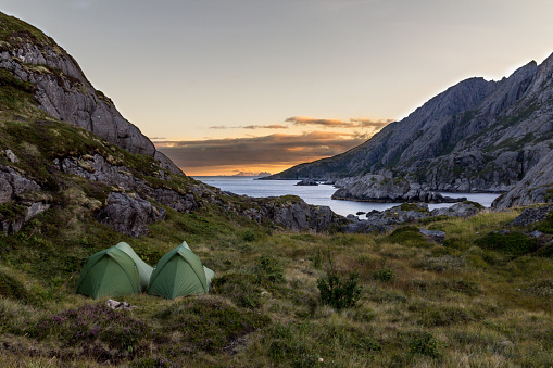 two green little camping tents next to the ocean with mountains in the background on the Lofoten Islands in Norway during sunset