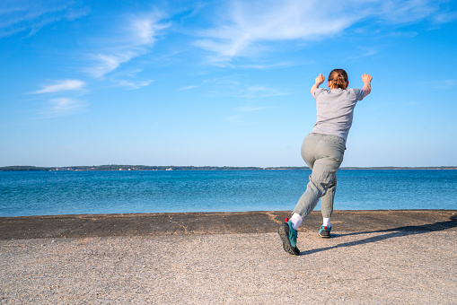 Back, side view of senior woman exercising on the beach in spring. Shi is in small place Peroj near Pula in Istria, Croatia with Brioni islands in horizon.