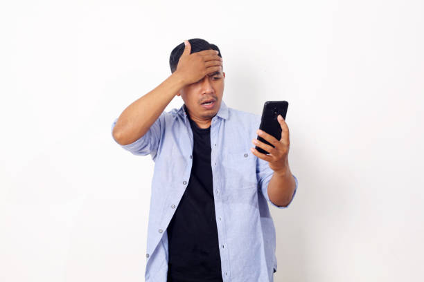 istock Young Asian man using smartphone stressed with hand on head, shocked with shame and surprise face, angry and frustrated over white wall background. Fear and upset for mistake. 1409029918