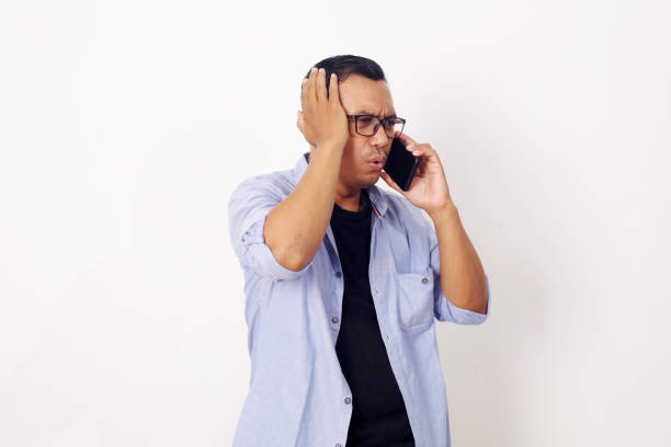 istock Young Asian man using smartphone stressed with hand on head, shocked with shame and surprise face, angry and frustrated over white wall background. Fear and upset for mistake. 1409034259