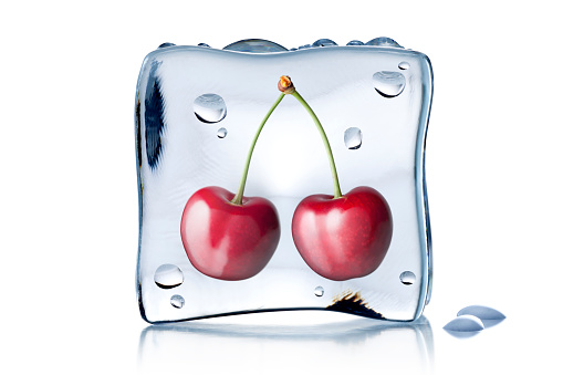 Cherries frozen in an ice cube isolated on white background.