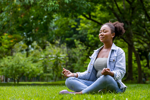 African American woman relaxingly practicing meditation in the forest to attain happiness from inner peace wisdom for healthy mind and soul concept