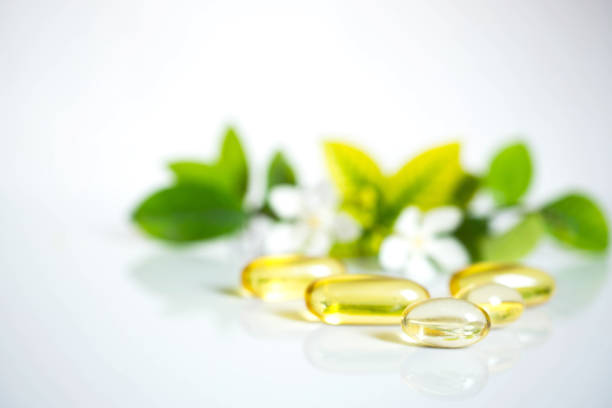 Close up soft capsules with leaves and white flora on white background with copy space for text.