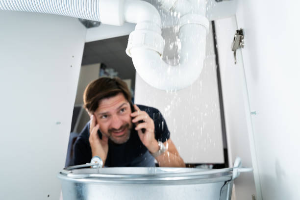 Worried Man Calling Plumber Worried Man Calling Plumber While Watching Water Leaking From Sink plumbing disaster stock pictures, royalty-free photos & images