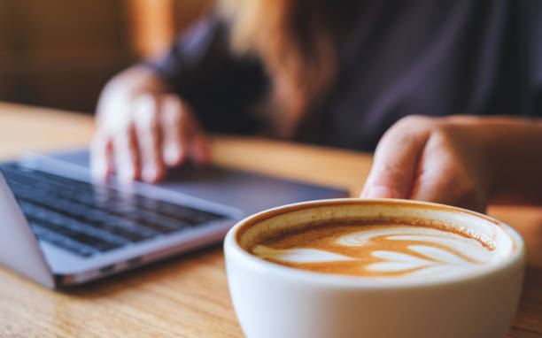 istock Closeup image of a woman holding and drinking hot coffee while working on laptop computer 1409045486
