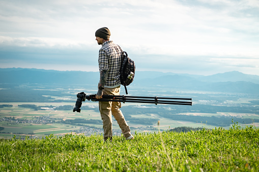 Landscape photographer working with tripod in beautiful green nature, walking on top of the hill.