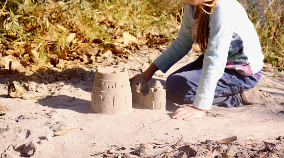 Child building sandcastle, playing with fun on the beach with toys. Autumn or springtime outdoors