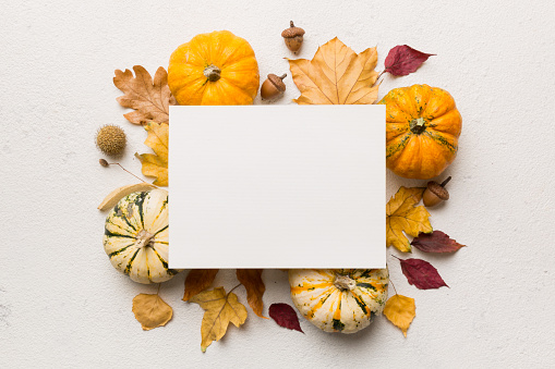 Autumn composition with paper blank and dried leaves with pumpkin on table. Flat lay, top view, copy space.