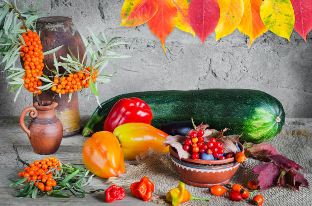 Autumn still life with sea buckthorn in a jug, vegetables, berries and colorful leaves on a rough gray background. Selective focus stock photo