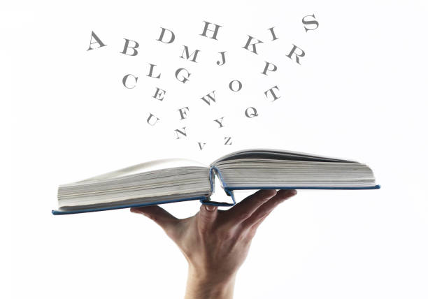 Hand holding opened book with flying, scattered letters  on white background. Education concept. stock photo