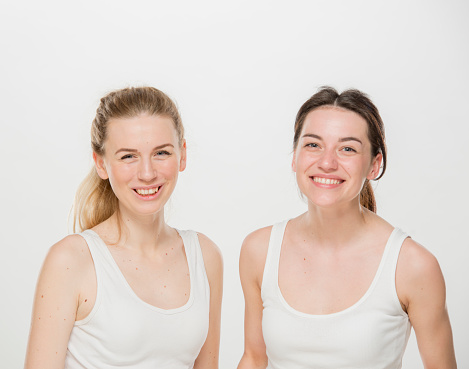 two girls are laughing.close-up portrait of two girls in white t-shirts on a white background isolated. two young Ukrainian girls, a brunette and a blonde, laugh merrily.