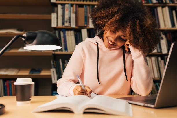 istock Smiling student in casuals sitting at table in library preparing her assignments 1409065130