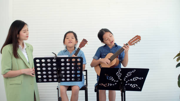 Happy Asian two siblings learning play skill guitar togetherness with teacher woman in classroom.Professional teacher training skill hold chords acoustic guitar student.Hobby education musical concept feliz asiático dos hermanos aprendiendo a tocar la guitarra habilidad juntos con la mujer maestra en el aula. habilidad de formación profesional de profesores de acordes de guitarra acústica estudiante. concepto musical de educación de pasatiempos